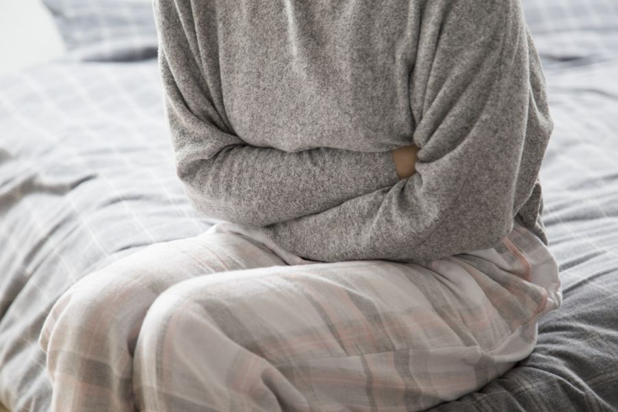 Pessoa sentada na cama segurando o abdômen em sinal de dor
